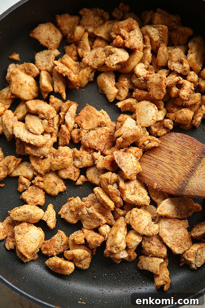 A skillet filled with bite-sized chicken taco meat with a wooden spatula inserted at an angle.
