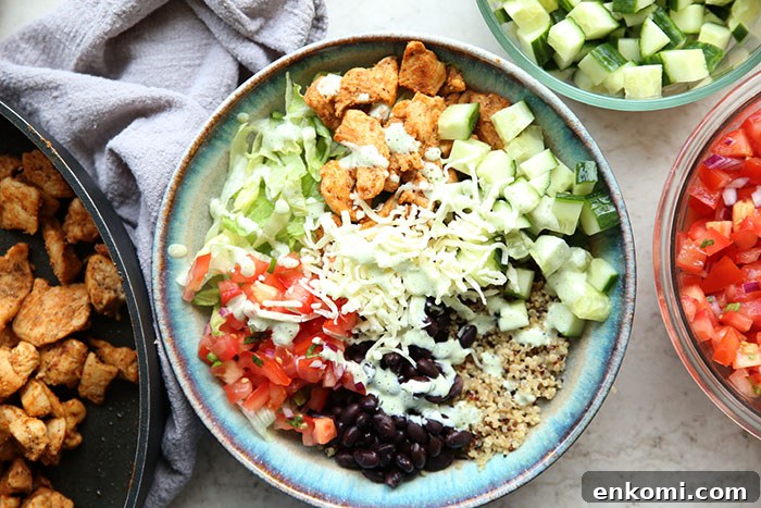 A bowl filled with quinoa, diced chicken taco meat, cucumbers, tomatoes, lettuce, black beans and topped with shredded cheese.