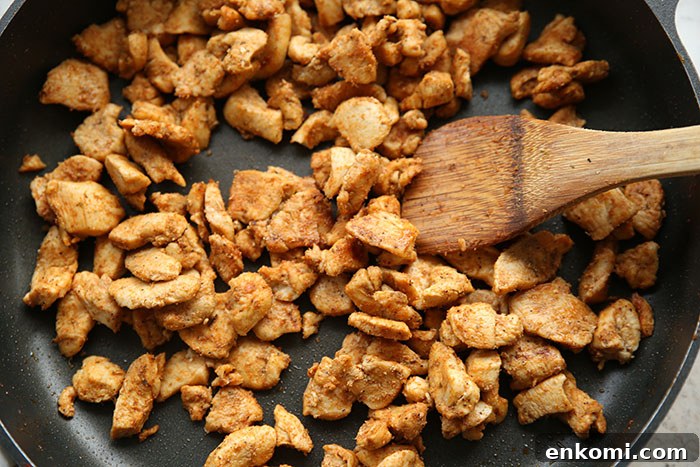 Bite-size chicken taco meat in a nonstick skillet with a wooden spatula.