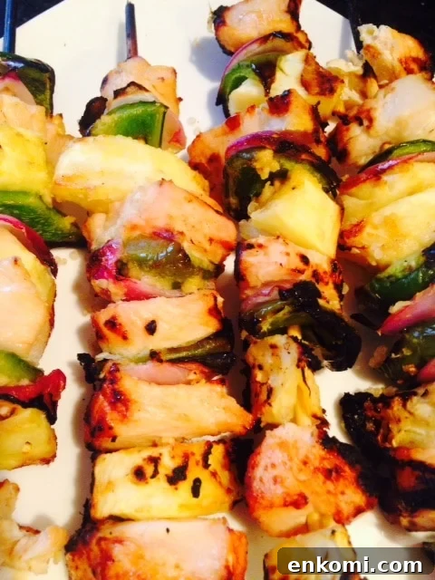 Diced chicken, pineapple, green pepper, and red onion are threaded on skewers and grilled, laying in a line on a plate