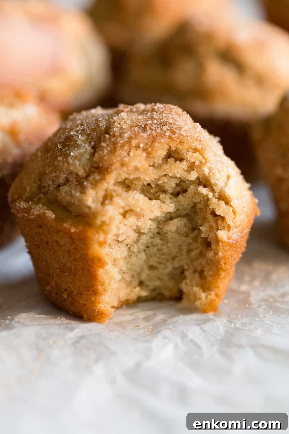 A Maple Donut Muffin on parchment paper with a bite taken out of it 