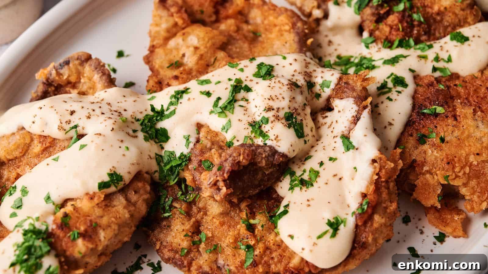 31 Spring Dinners That Feel Fresh, Not Fussy 13 Breaded and fried steak pieces topped with creamy white gravy and chopped parsley on a white plate.