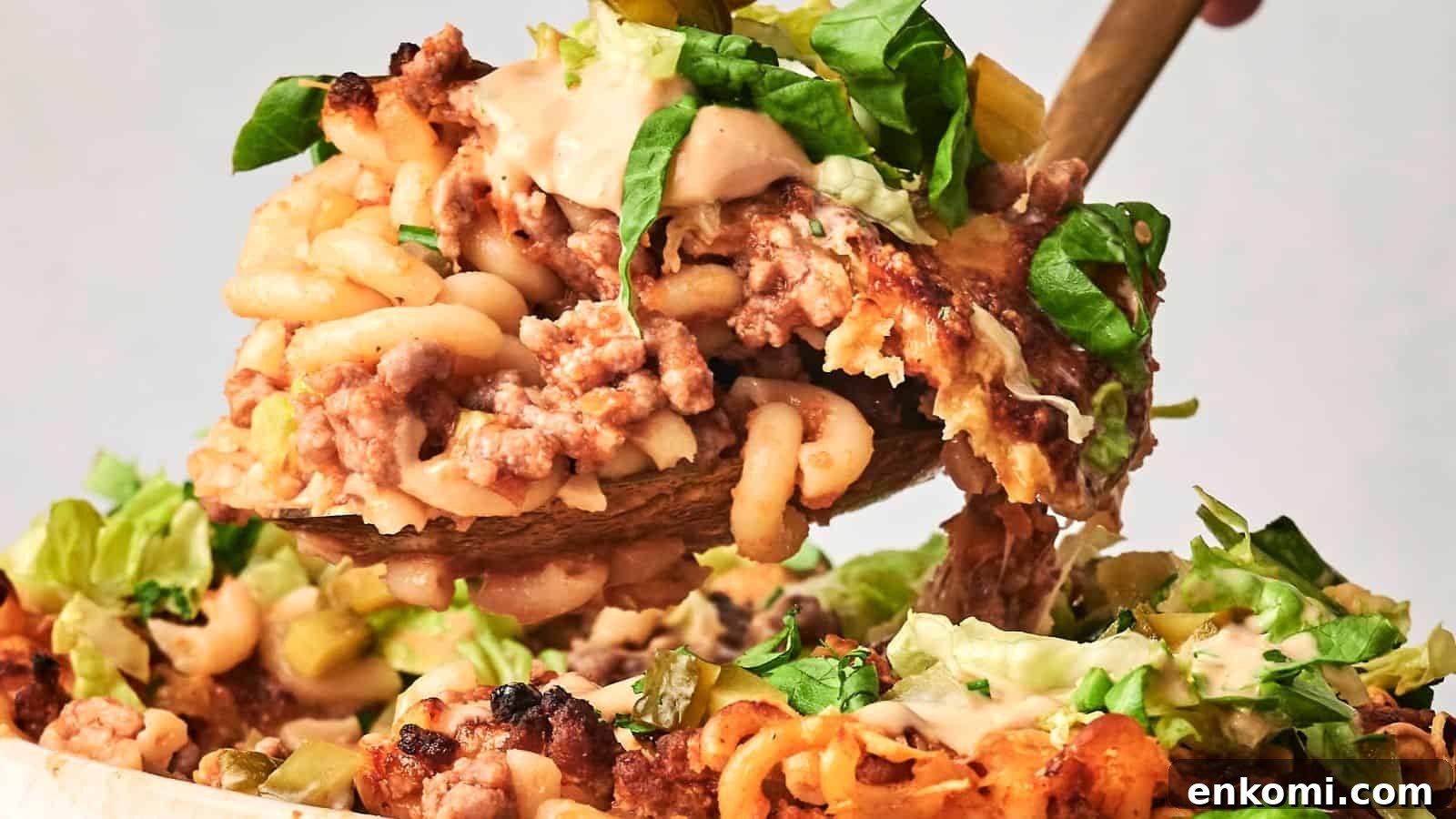 31 Spring Dinners That Feel Fresh, Not Fussy 26 A close-up of a spoon lifting a portion of hamburger casserole, showcasing baked macaroni and cheese layered with ground meat and topped with lettuce and creamy sauce.