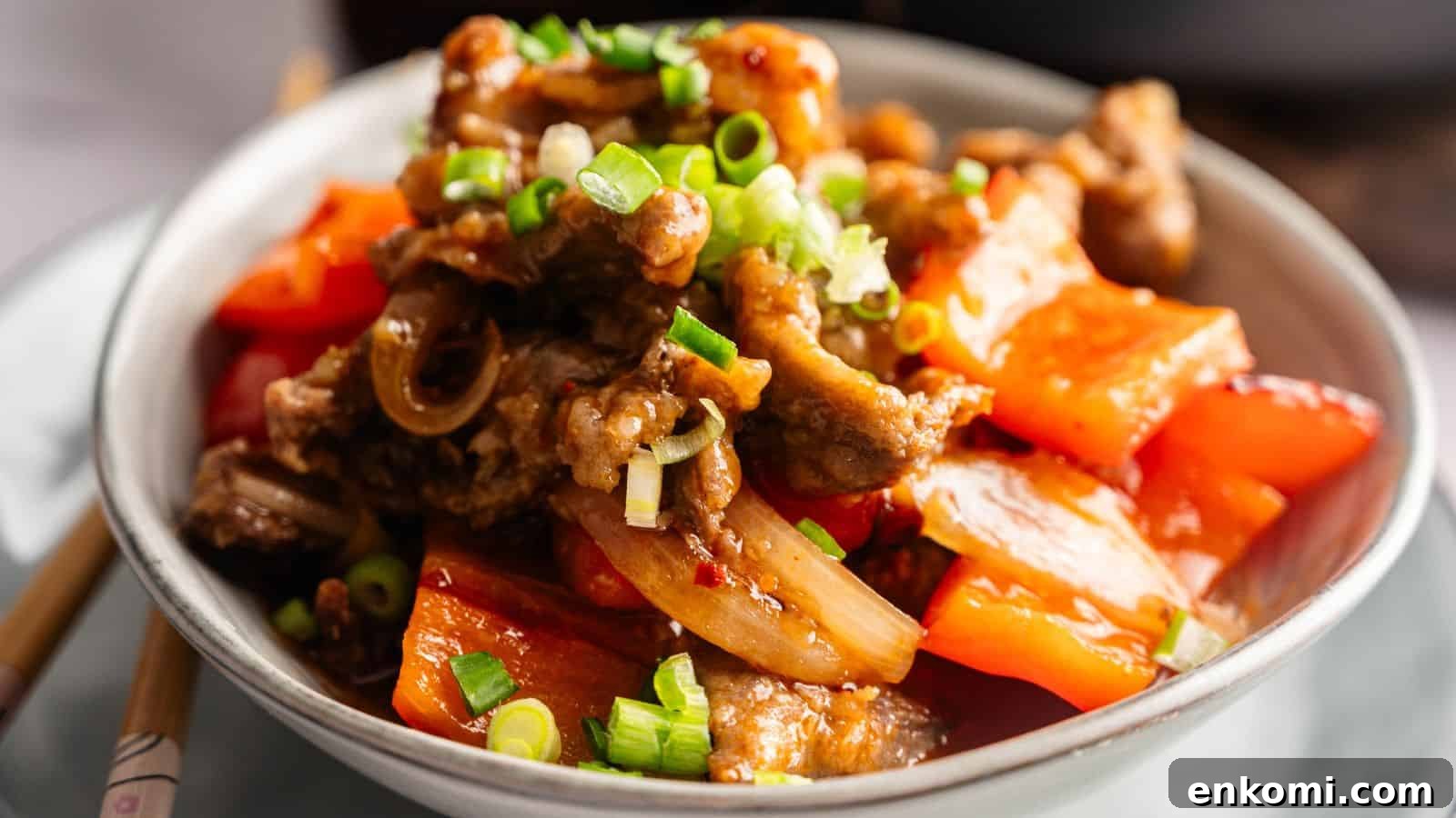 31 Spring Dinners That Feel Fresh, Not Fussy 33 A bowl of stir-fried beef with red bell peppers, onions, and chopped green onions, served on a white plate.
