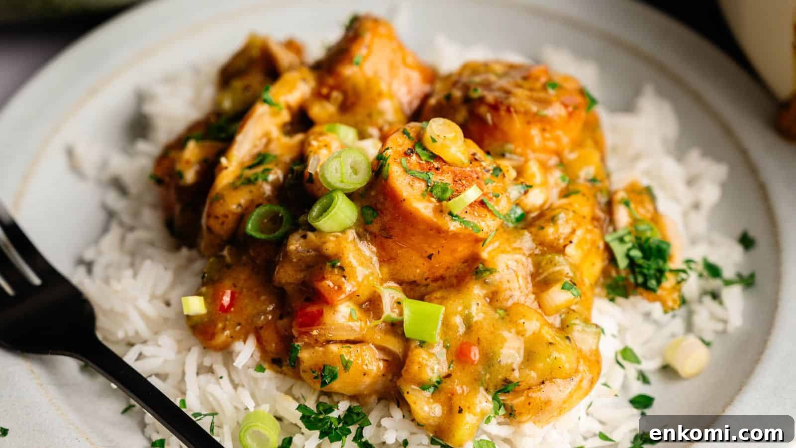 31 Spring Dinners That Feel Fresh, Not Fussy 10 A plate of white rice topped with chunks of chicken in a yellow curry sauce, garnished with chopped green onions and herbs. A black fork is placed on the side.