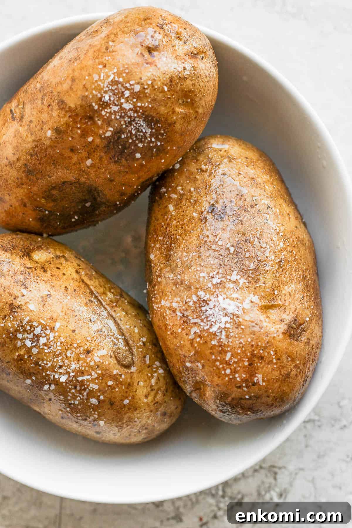 Twice-Baked Potatoes with Cheddar and Crispy Bacon 3 Whole baked potatoes in a white bowl.