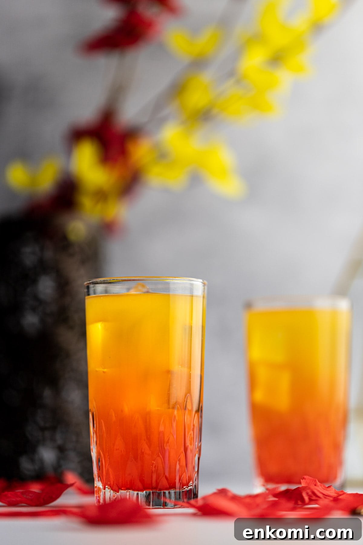 Amaretto Sunrise Cocktail Recipe with Orange and Cherry 2 Two glasses of ombre amaretto sunrise cocktails, with red on the bottom and yellow on top, with yellow and red flowers in the background.