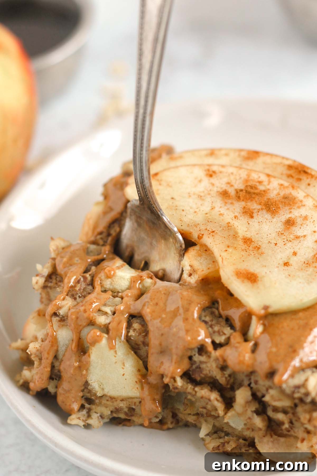 Warm Apple Cinnamon Baked Oatmeal with Crunchy Topping 8 Fork taking a bite out of a square piece of apple baked oatmeal topped with sliced apples and almond butter.