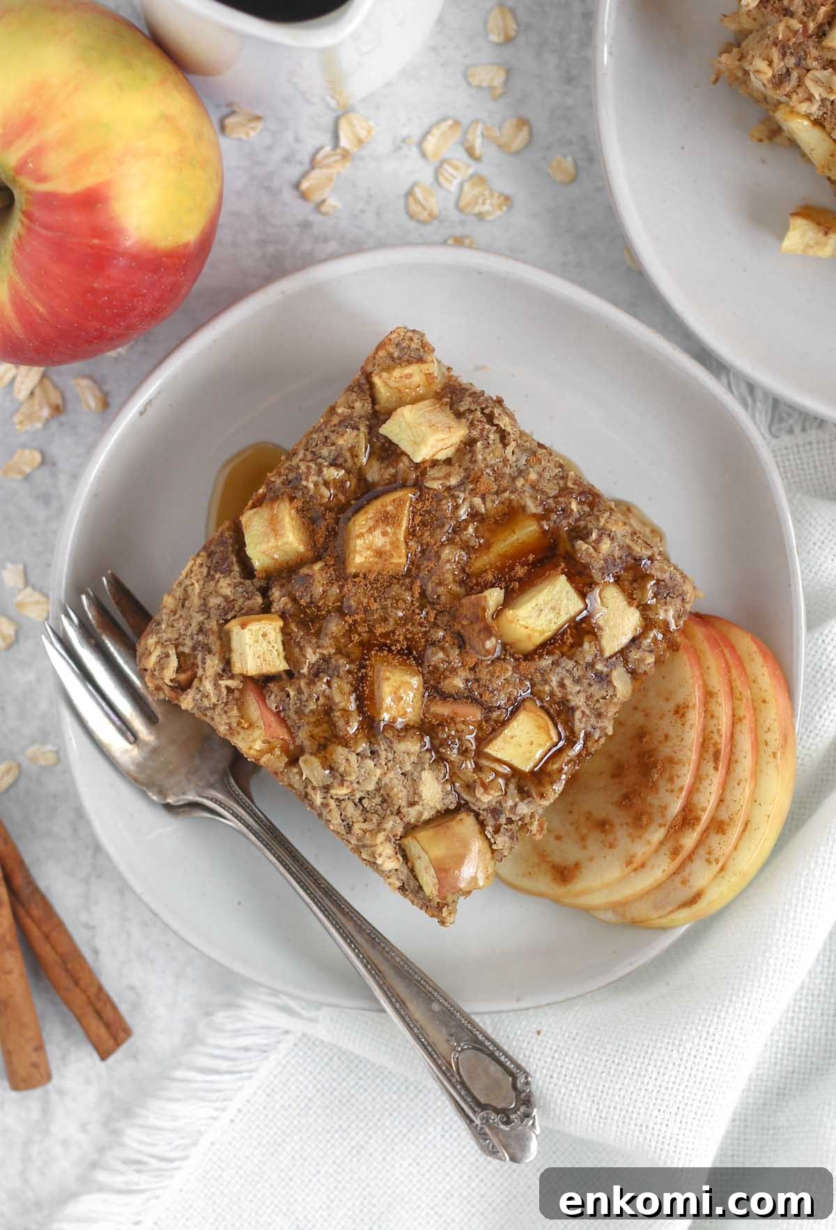 Warm Apple Cinnamon Baked Oatmeal with Crunchy Topping 9 Square piece of apple cinnamon baked oatmeal topped maple syrup on a round plate with a vintage fork.