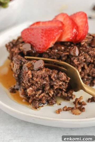 Gold fork cutting a bite off of a piece of chocolate baked oats topped with strawberries.
