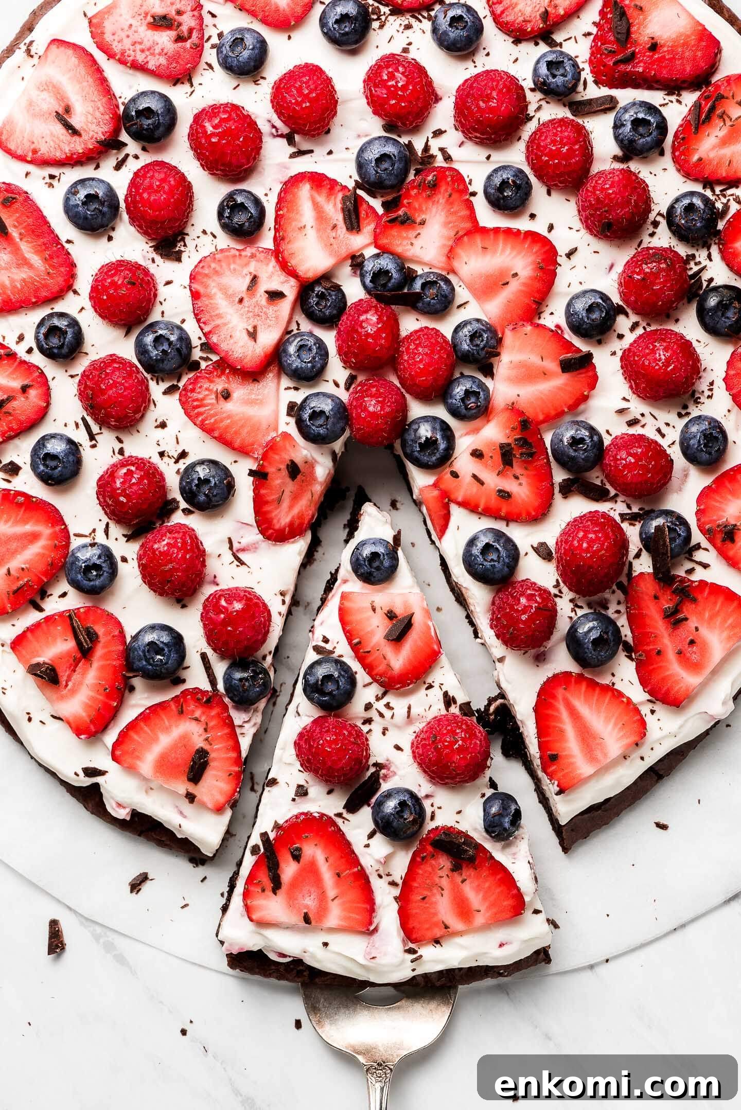 Berry Brownie Pizza decorated with strawberries, raspberries, and blueberries with a slice cut out and being pulled away.