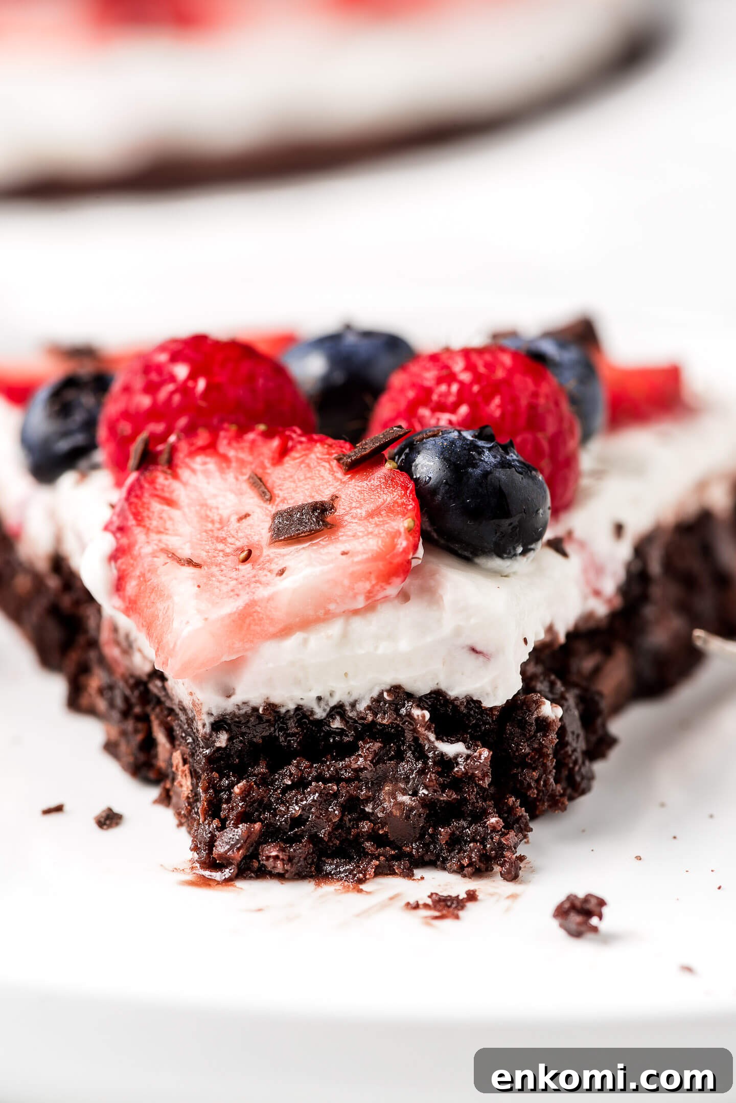 A close up shot of a fudgy brownie covered in cream cheese whipped topping and berries.