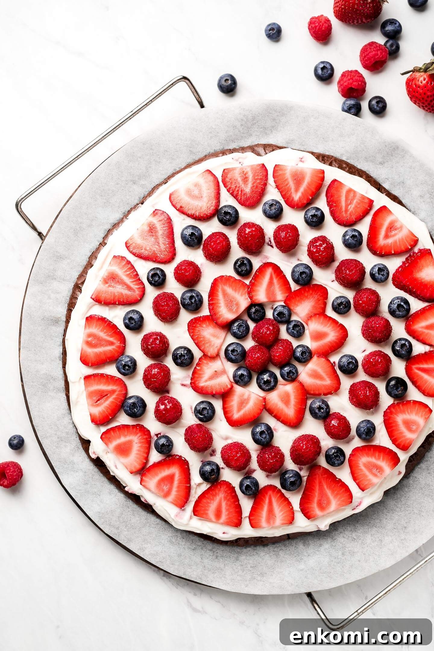A brownie fruit pizza on a parchment lined pizza stone.