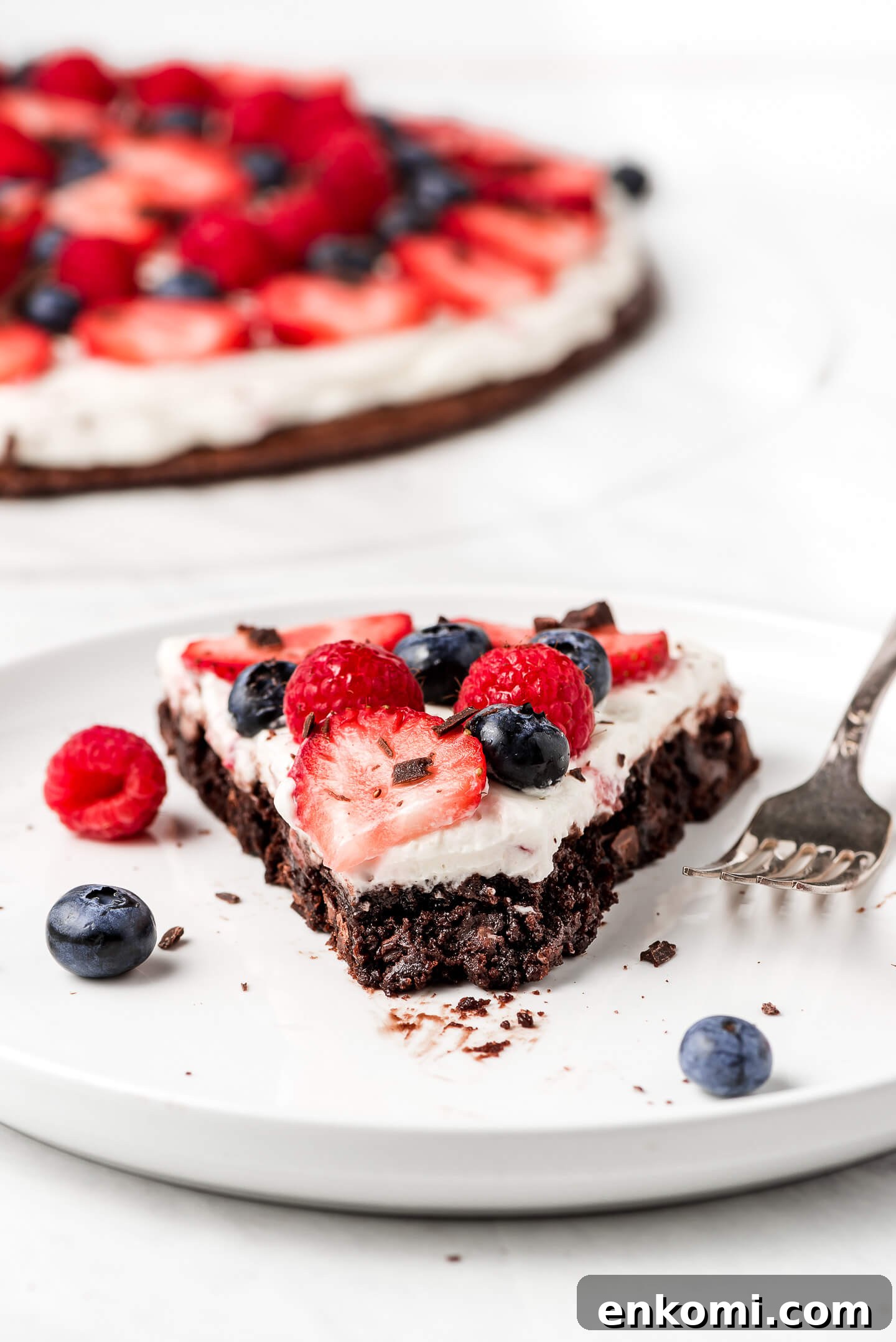 A slice of Brownie Pizza topped with a cheesecake spread and fresh berries.