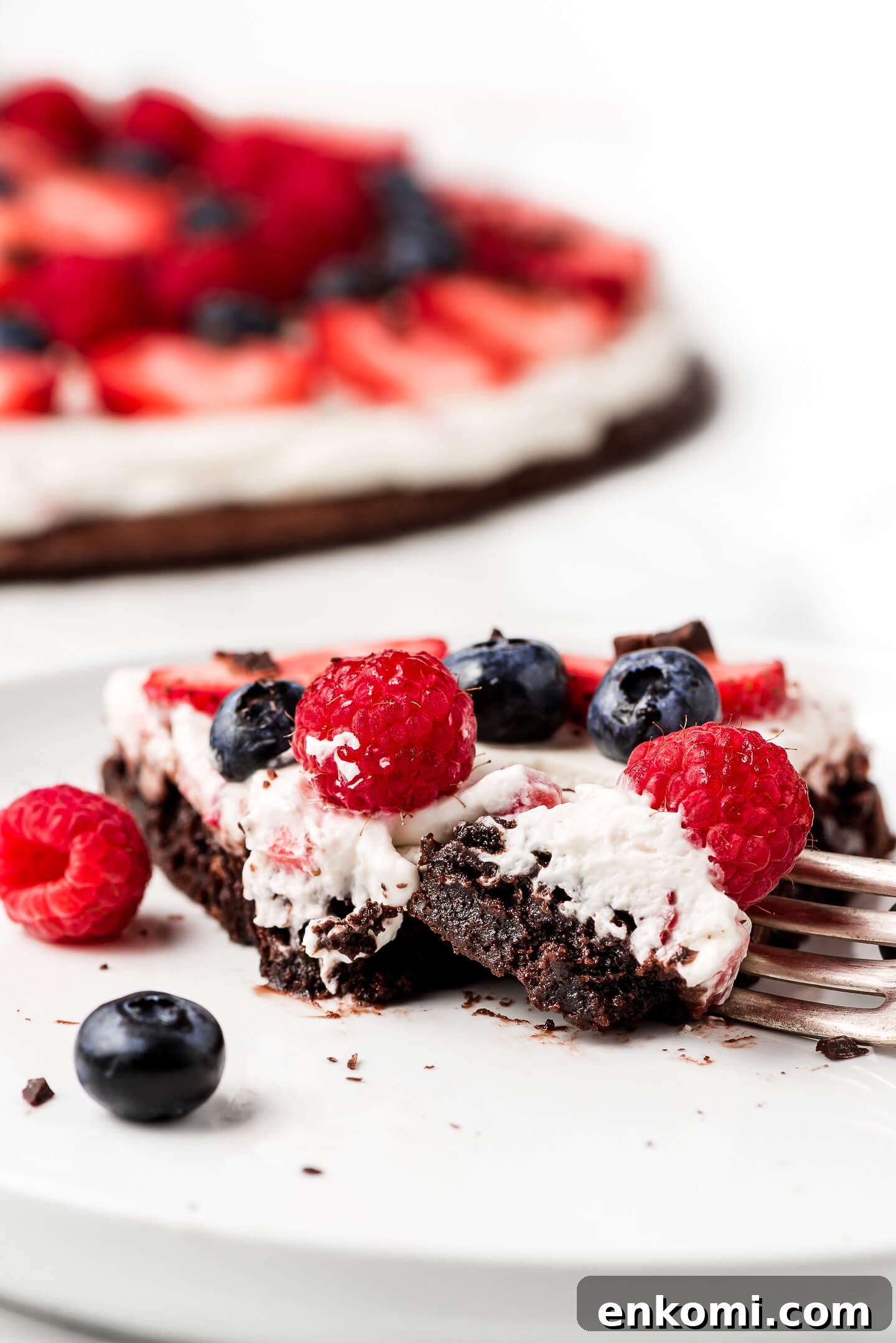 A slice of Berry Brownie Pizza on a plate with a fork cutting into it.