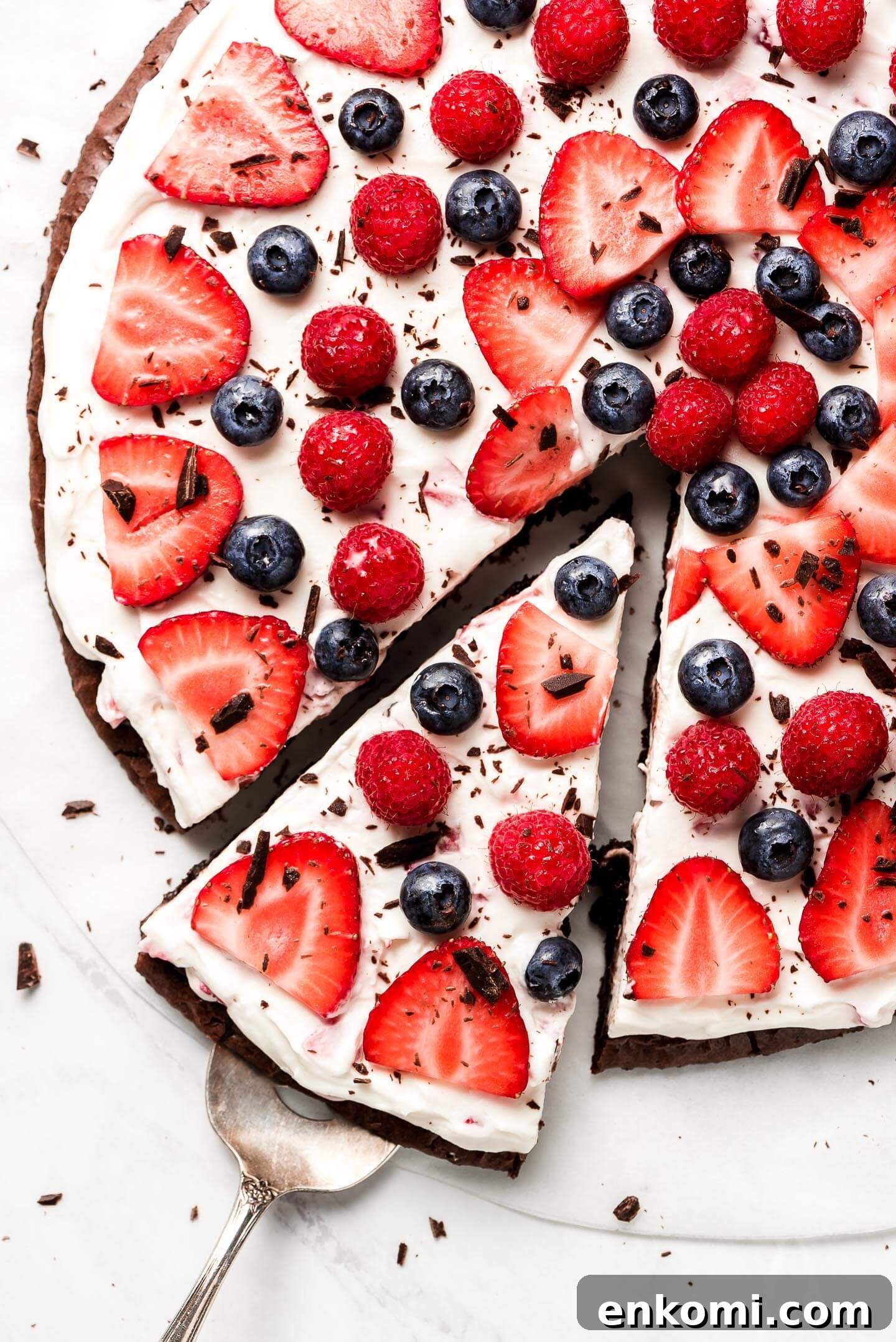 A close up shot of the top of a brownie pizza covered in fresh sliced strawberries, raspberries, and blueberries and sprinkled with finely chopped chocolate.