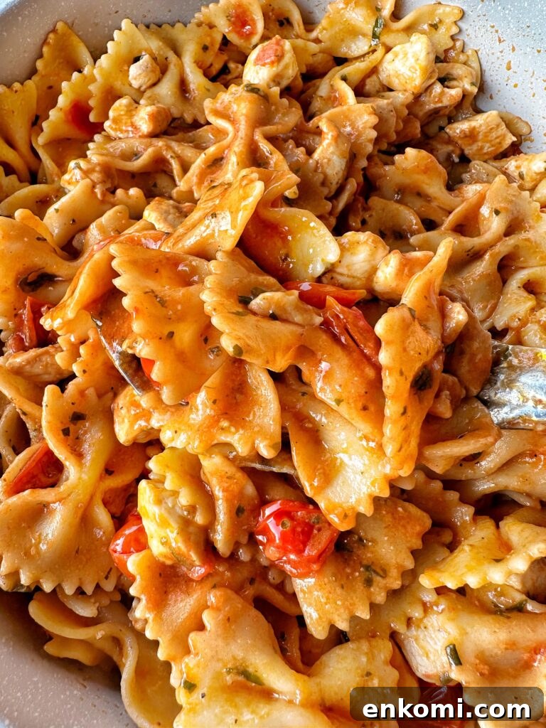 A close up view of bow tie pasta with chicken and tomato pieces