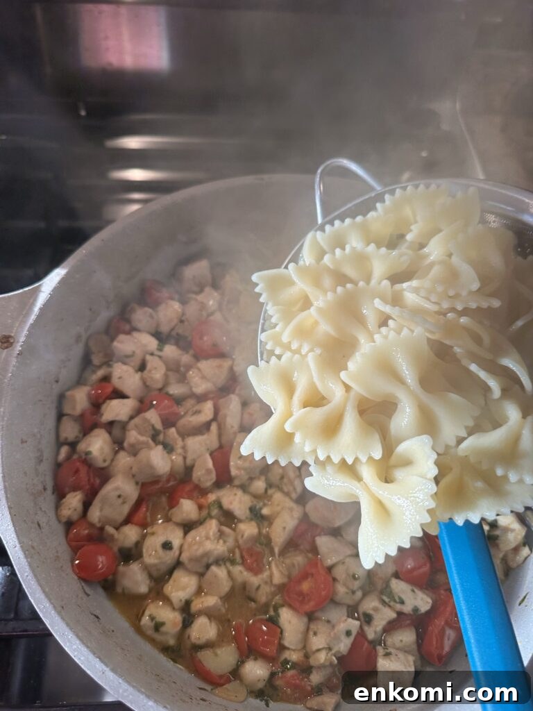 Pasta held in a strainer over pieces of chicken and tomato cooking in a pot