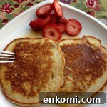 Two pancakes on a white plate with sliced strawberries.