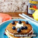 Stack of pancakes on a blue plate with blueberries and butter on top.