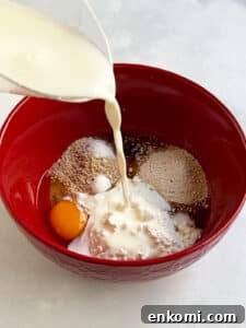 Pouring milk into cheese latke ingredients in a medium red bowl.