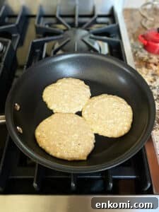 Three pancakes unflipped in a small fry pan on the stove.