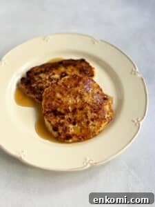 Two cheese latkes on an off white plate with syrup on top.