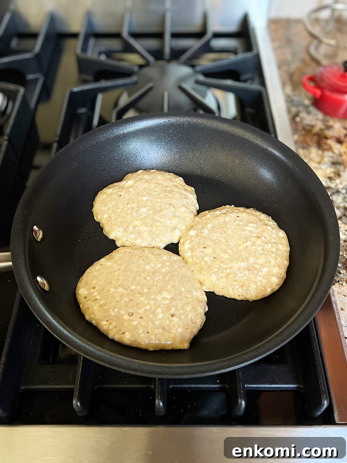 Three cheese latkes in a pan cooking with the uncooked side facing up.