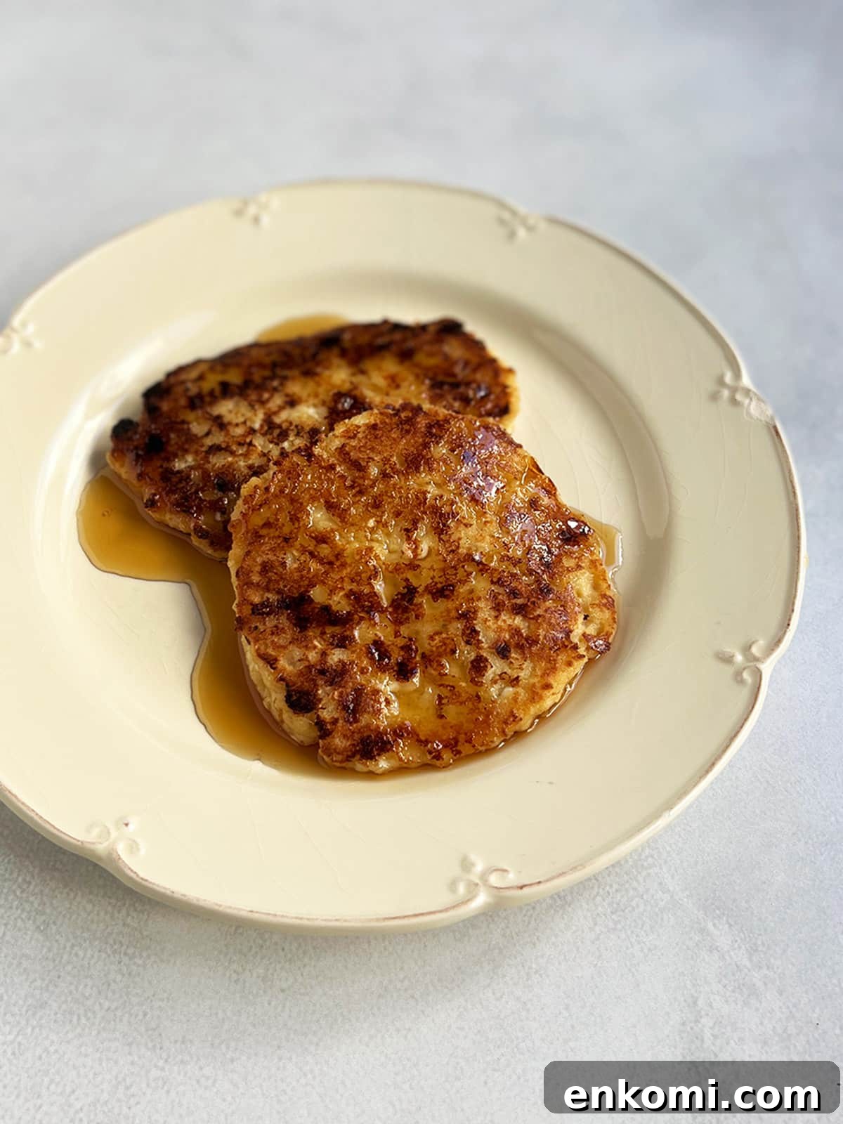 Two cheese latkes on an off white plate with maple syrup poured on top.