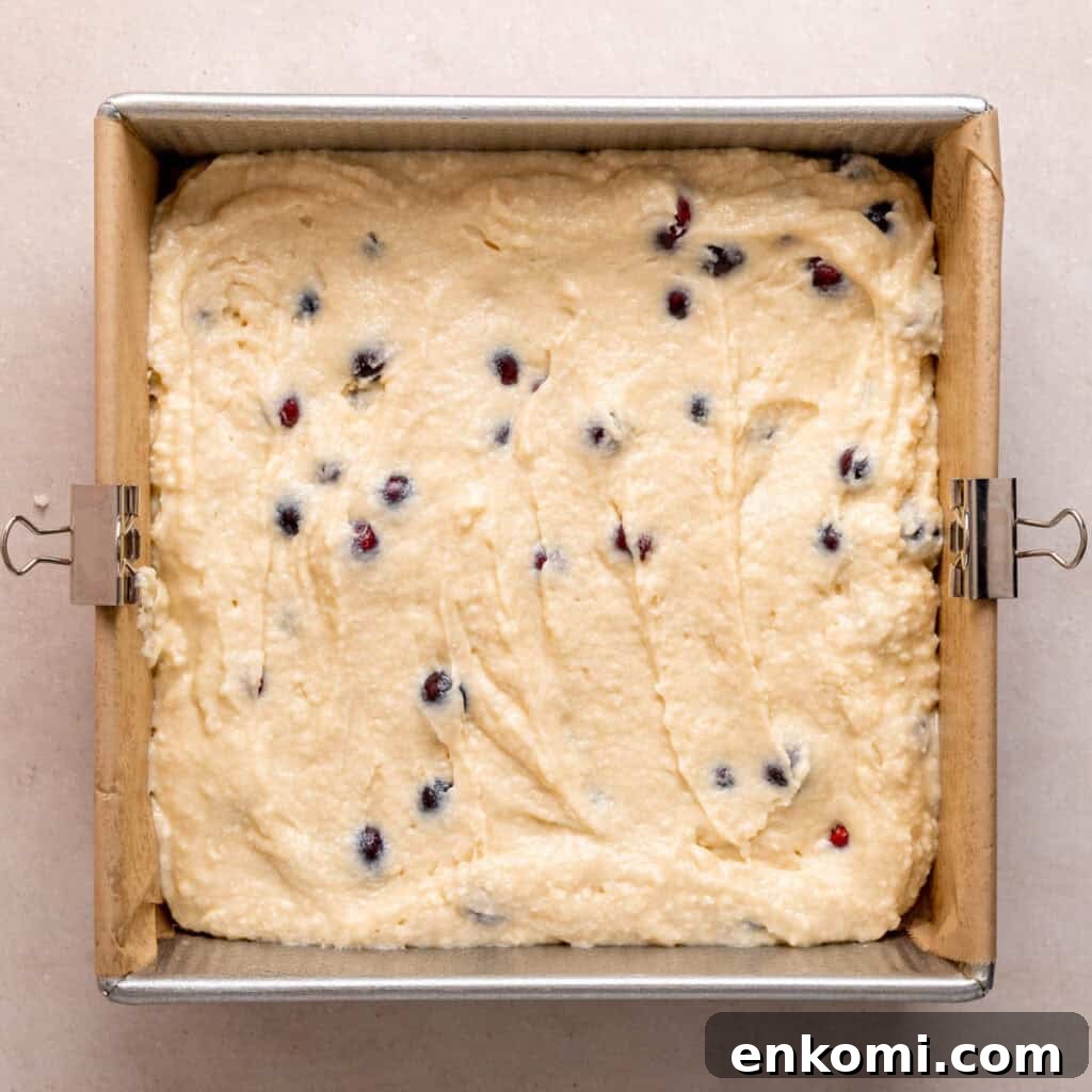 A parchment-lined square cake pan filled with cranberry coffee cake batter.