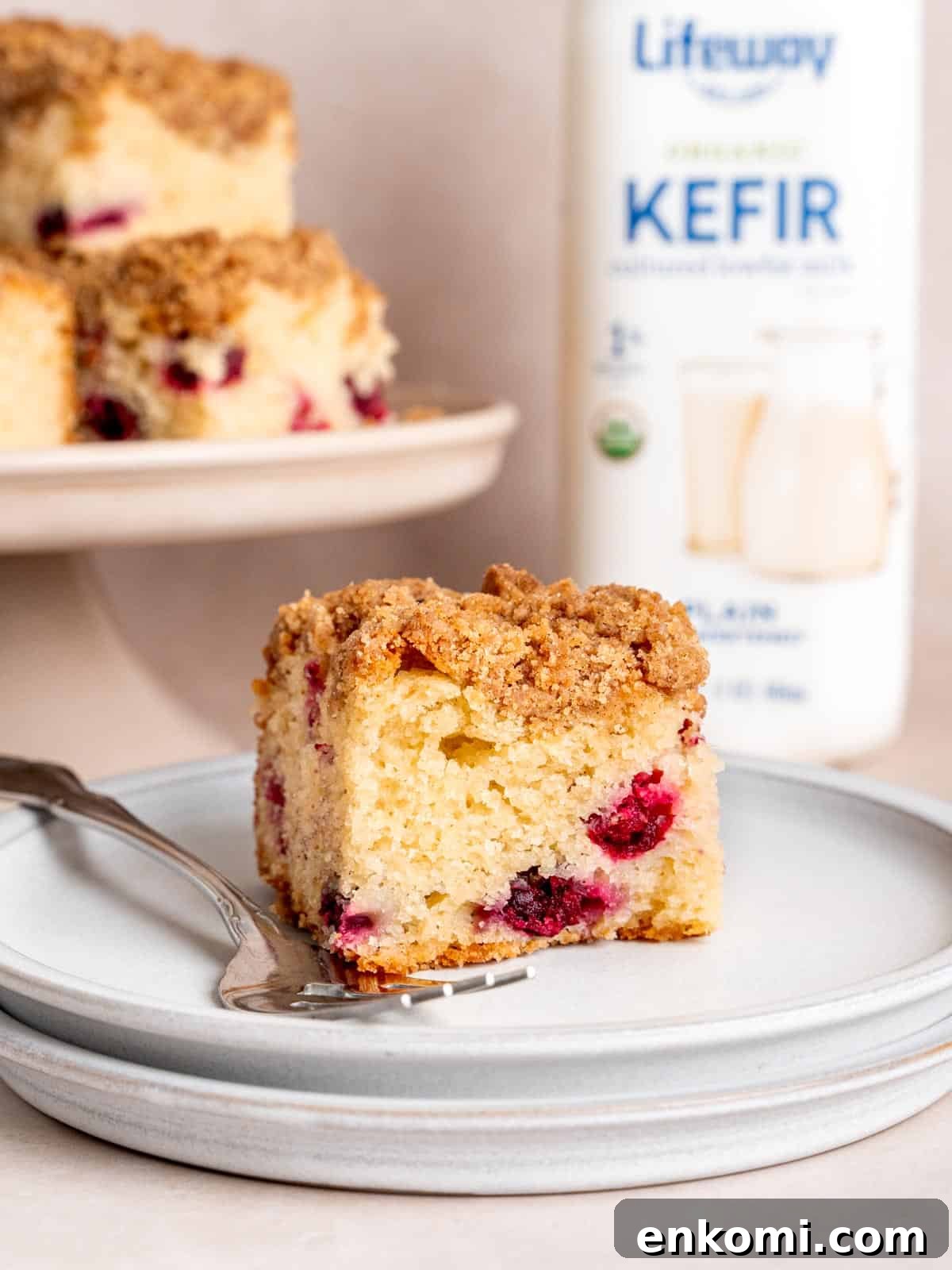A slice of cranberry coffee cake on a plate next to a bottle of kefir.