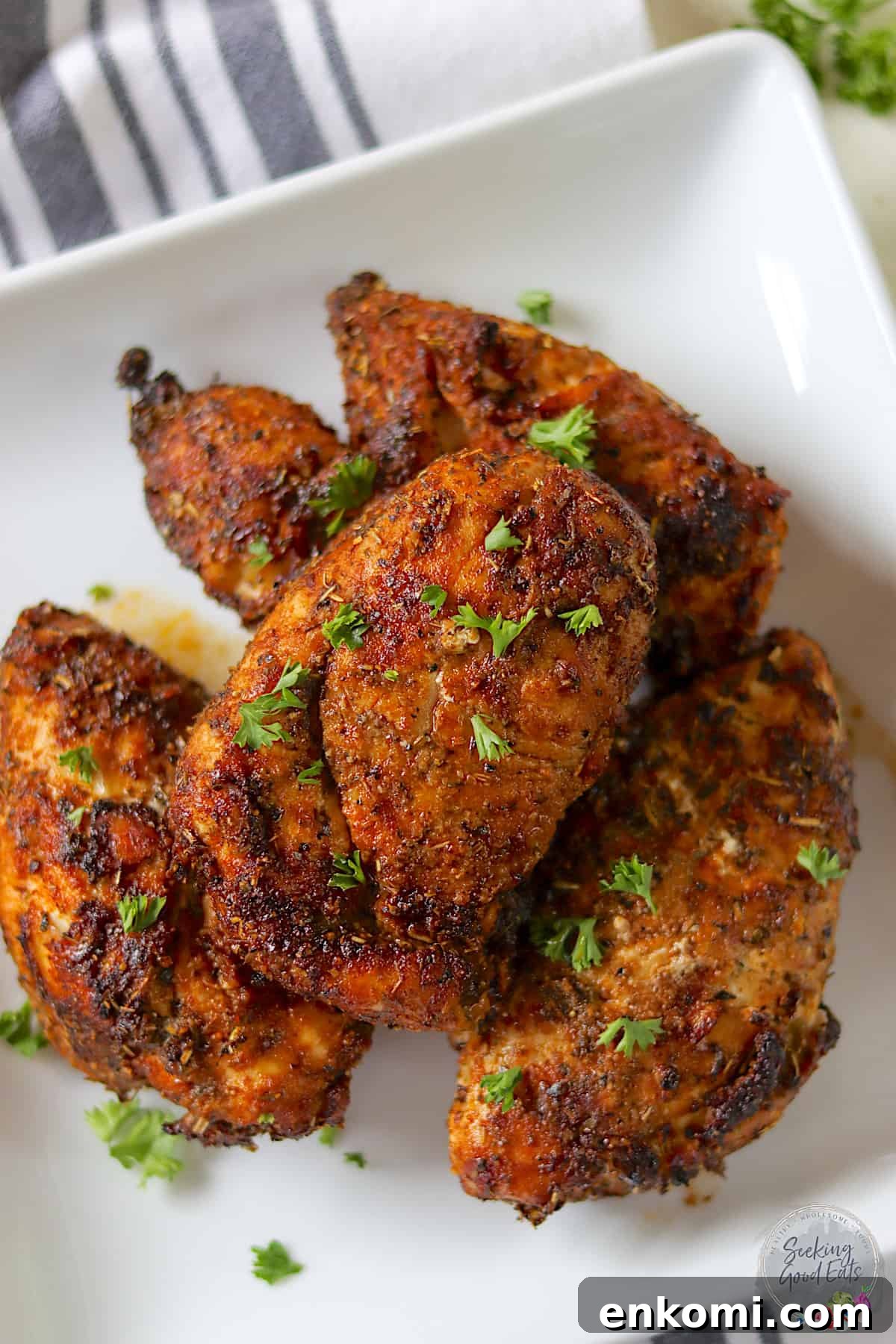 Four air fryer chicken breasts on a square white plate garnished with parsley.