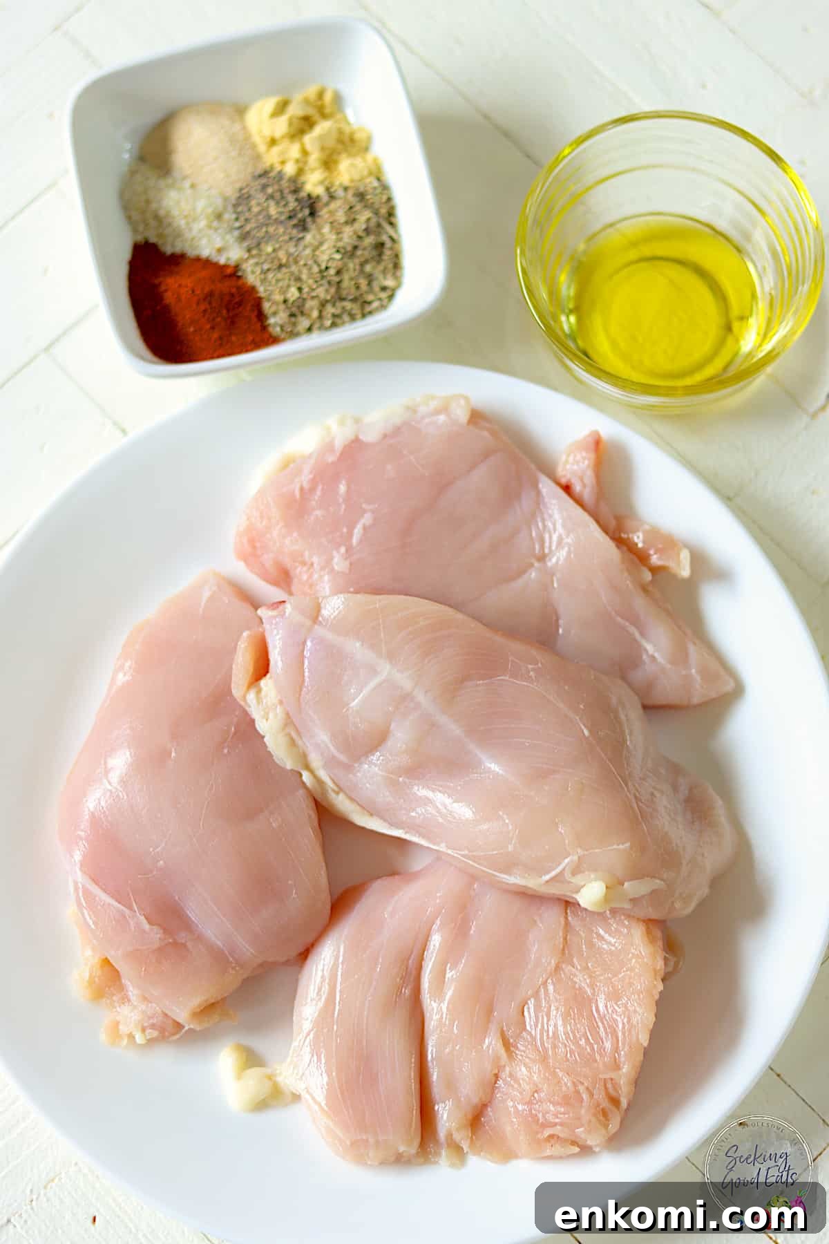 Ingredients needed for making air fryer chicken breasts on a wooden white table.