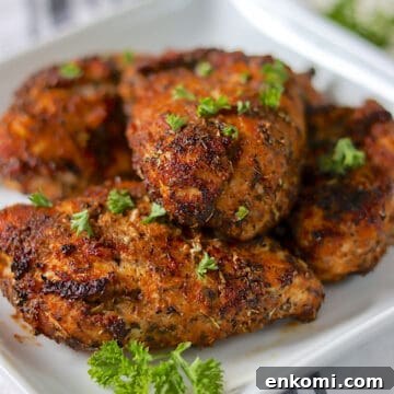 Golden air fried chicken breasts on a white plate garnished with fresh parsley.