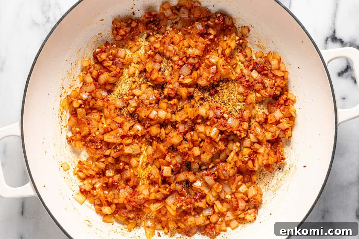 Large pan filled with sauteed onion, garlic, spices, and tomato paste.