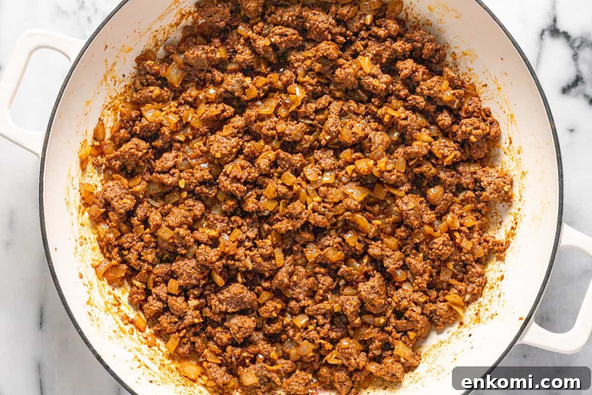 Large sauté pan filled with browned ground beef, onions, and spices.