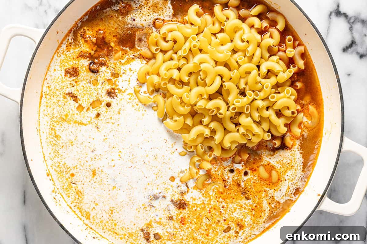 Large pan filled with heavy cream, macaroni noodles, broth, and sauteed veggies.