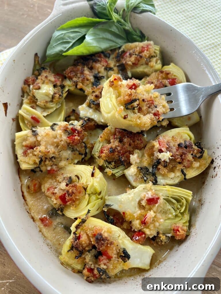 Oven-Roasted Italian Artichoke Hearts with Lemon Breadcrumbs 18 Piece of roasted Italian artichoke hearts oreganata with lemon basil breadcrumbs on fork over baking dish full of them with basil garnish.