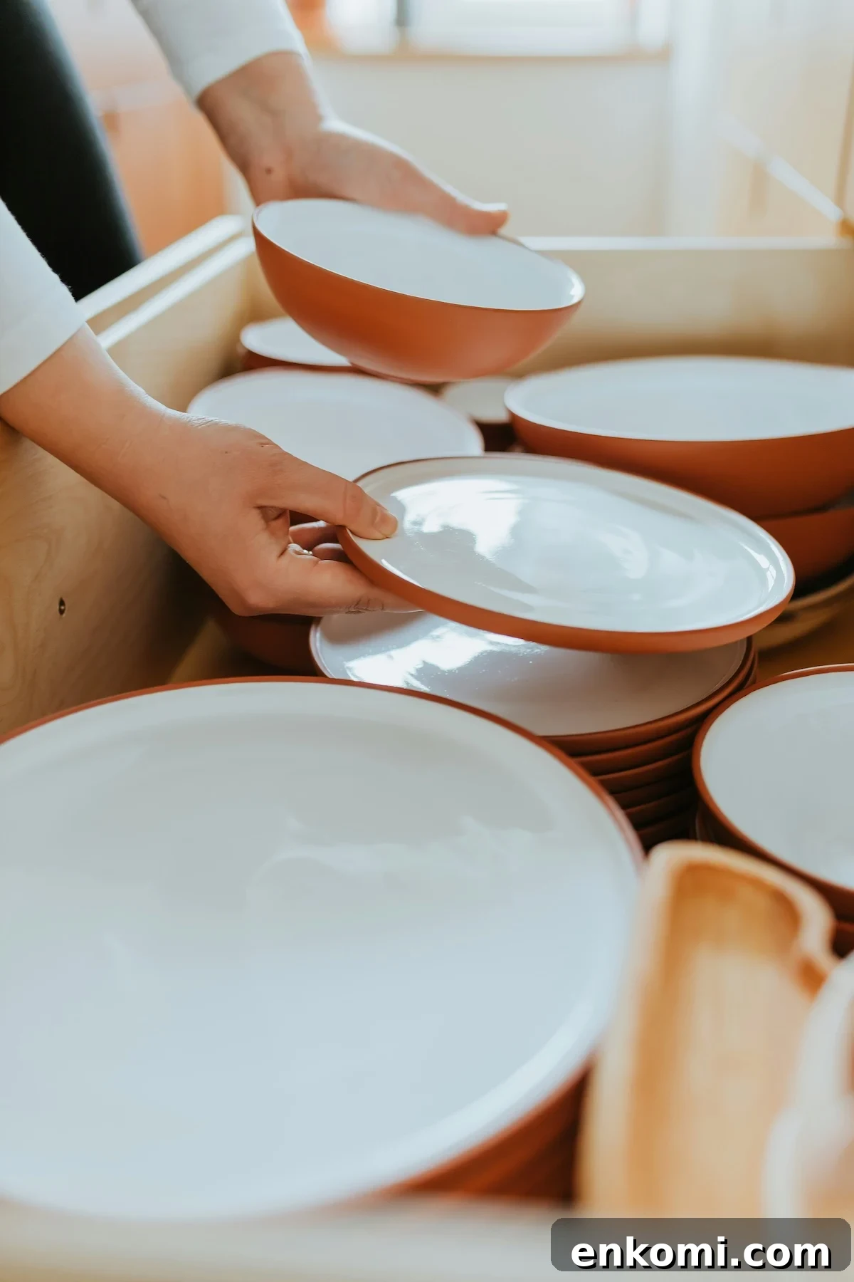 Closeup image of a woman's hands in a drawer full of dishes holding two plates like shes making decisions about what to declutter