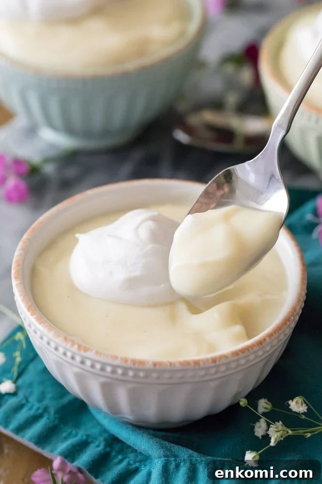 Spoon with vanilla pudding on it, bowl of vanilla pudding topped with whipped cream in the background