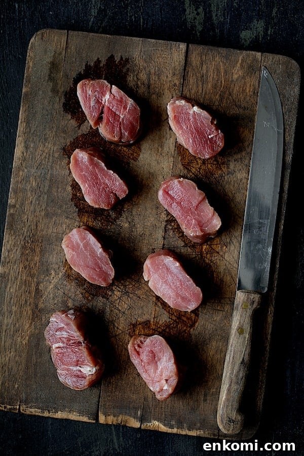 Spicy Tahini Pork Medallions with Harissa Sweet Potato Wedges 4 Photo of eight uncooked pork medallions on wood cutting board with knife.