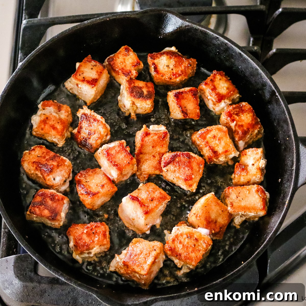 pork bites cooking in oil in a cast iron skillet.