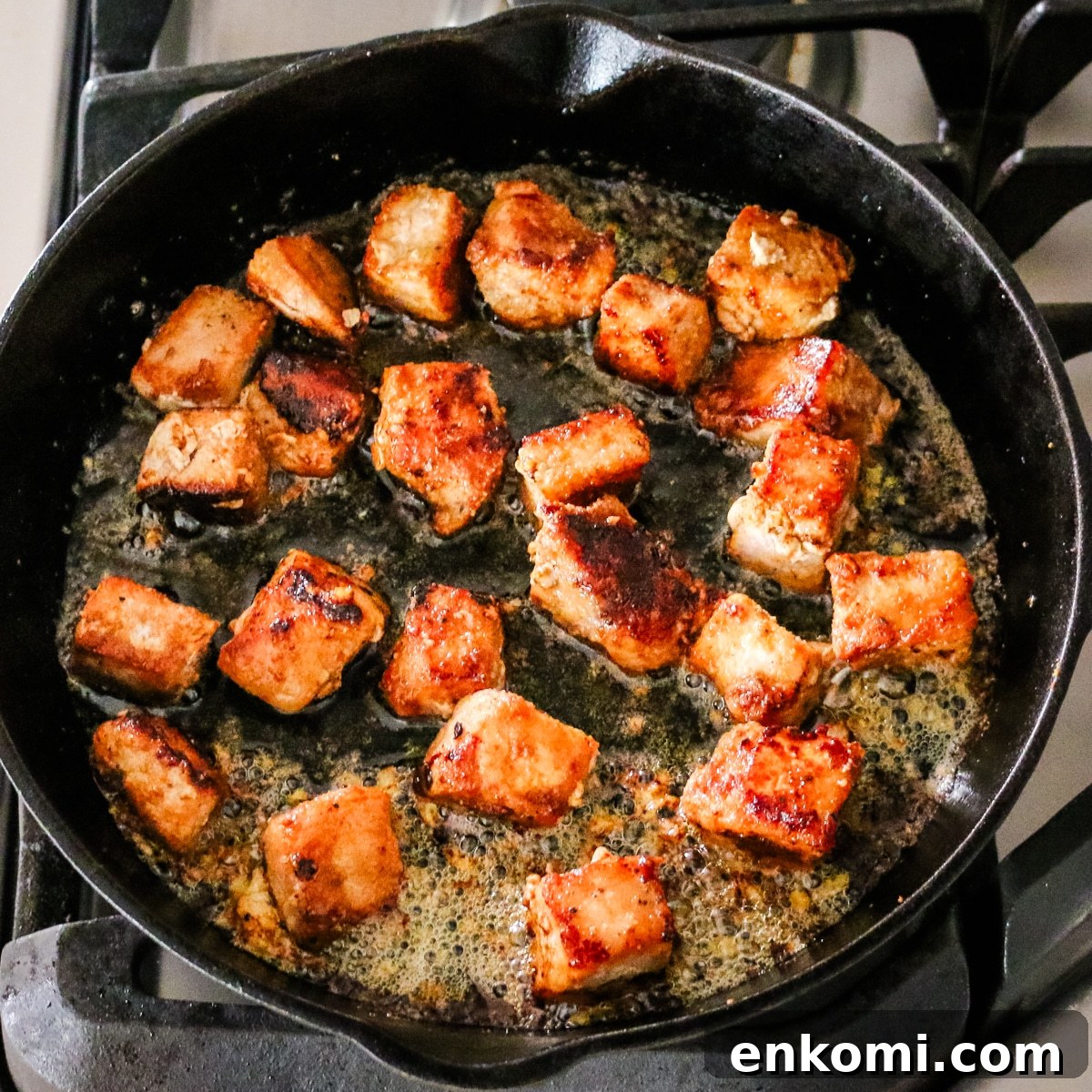 pork bites cooking in cast iron skillet.