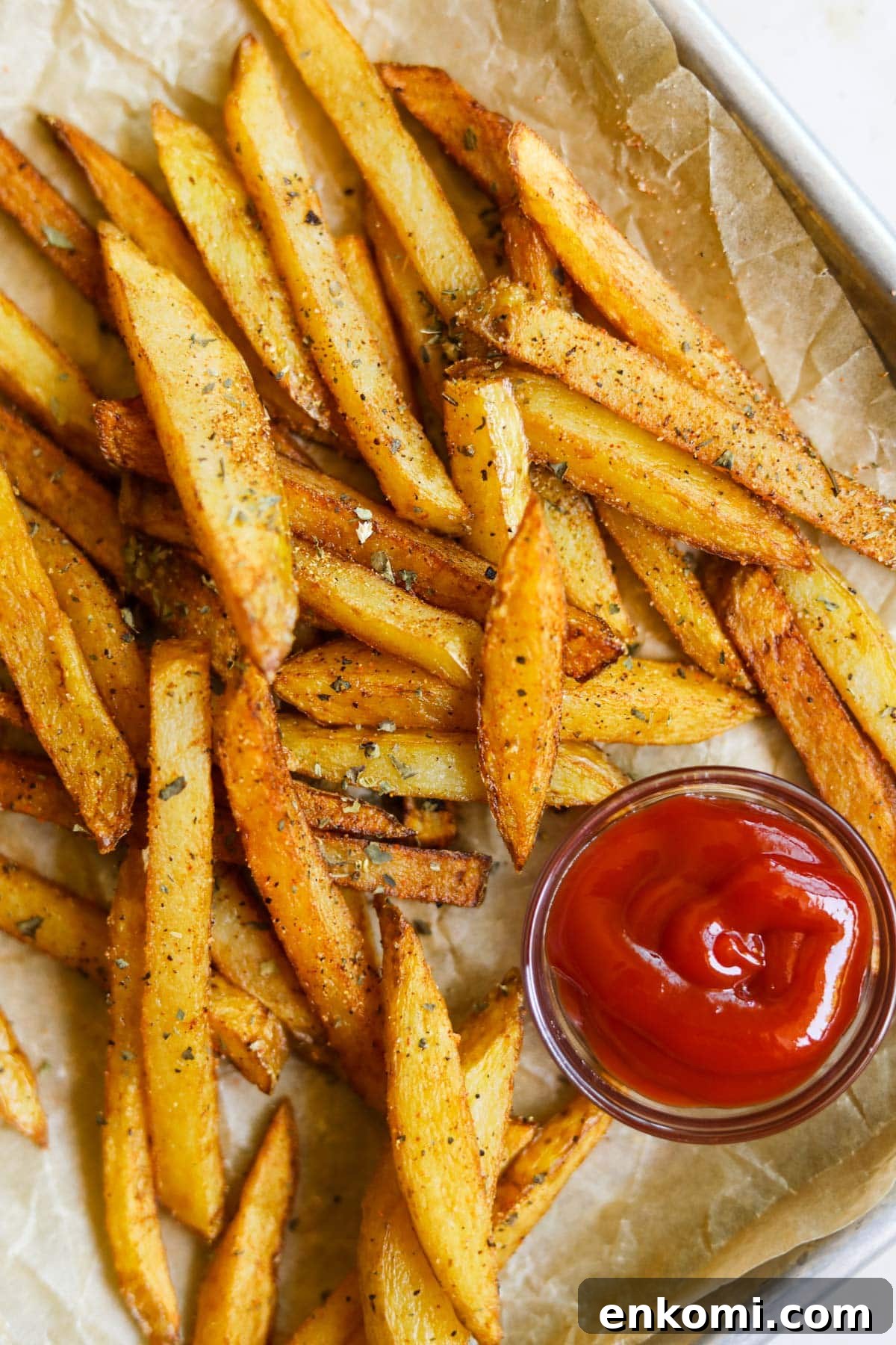 Crispy Homemade Seasoned French Fries 2 Classic seasoned french fries with garlic powder, dried basil, paprika, and ketchup on a baking sheet with parchment paper.