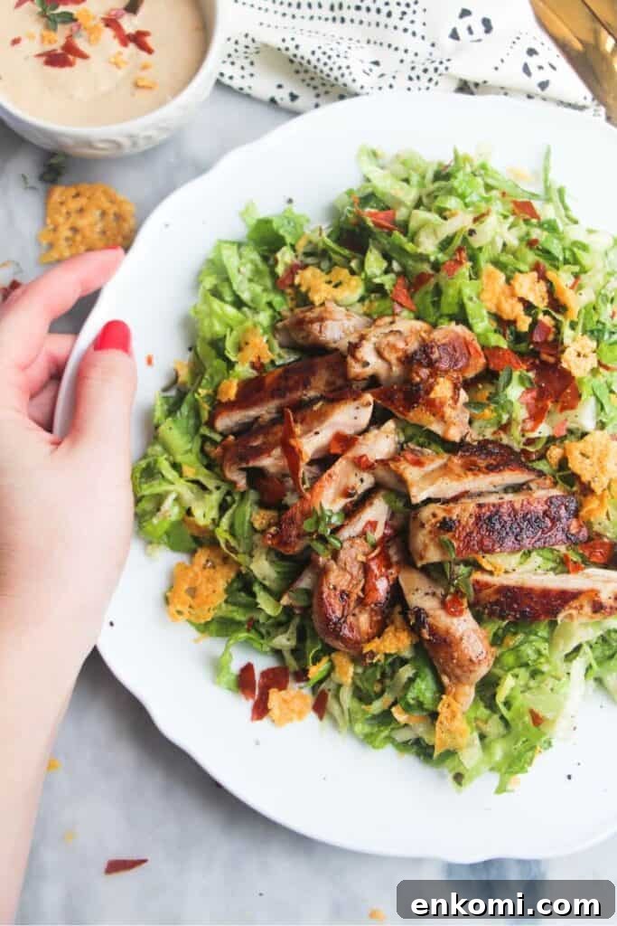 20-Minute Marry Me Chicken with Creamy Sun-Dried Tomato Sauce 15 A hand holding a large white plate with sliced grilled chicken on top of green chopped lettuce.