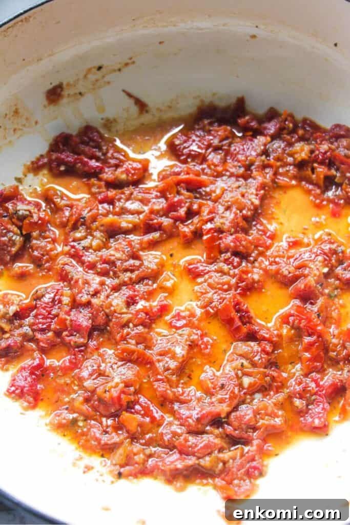 20-Minute Marry Me Chicken with Creamy Sun-Dried Tomato Sauce 6 Chopped sundried tomatoes cooking in a large white skillet.