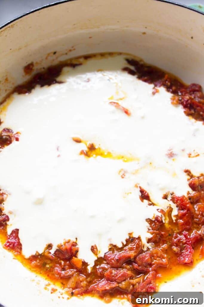 20-Minute Marry Me Chicken with Creamy Sun-Dried Tomato Sauce 7 Cream added to sundried tomatoes in a large white skillet.