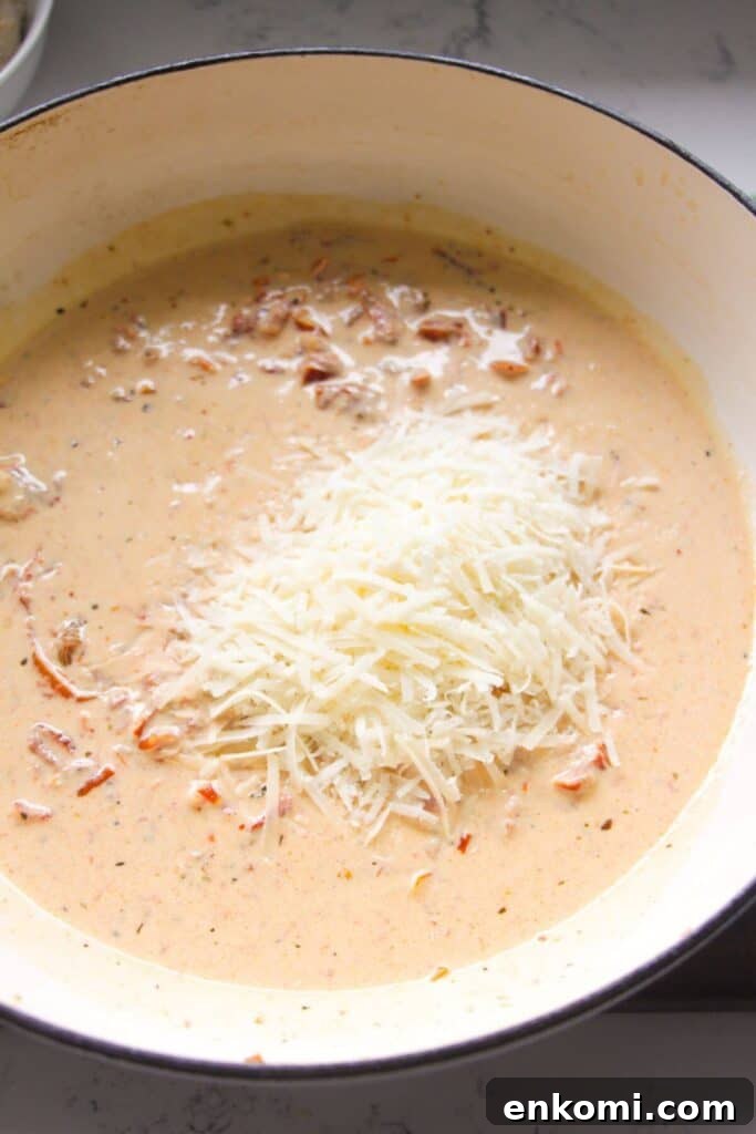 20-Minute Marry Me Chicken with Creamy Sun-Dried Tomato Sauce 8 Grated parmesan cheese added to creamy sundried tomato sauce in a large white skillet.