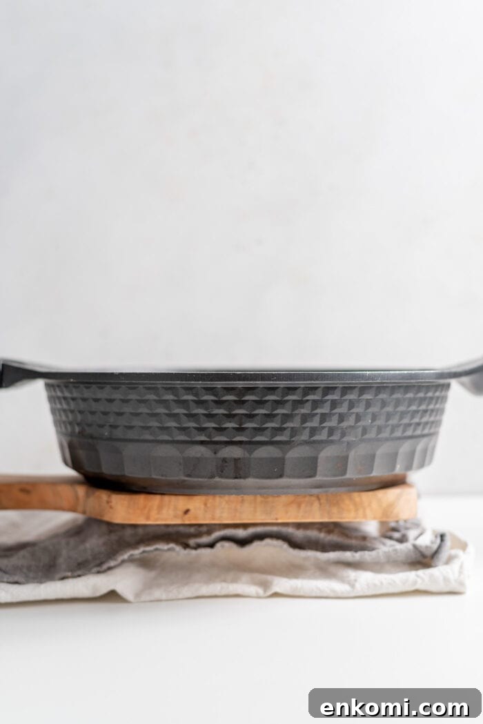 How to Press Tofu for Crispy, Firm Results 7 A black frying pan sitting on a block of tofu wrapped in a dish cloth.