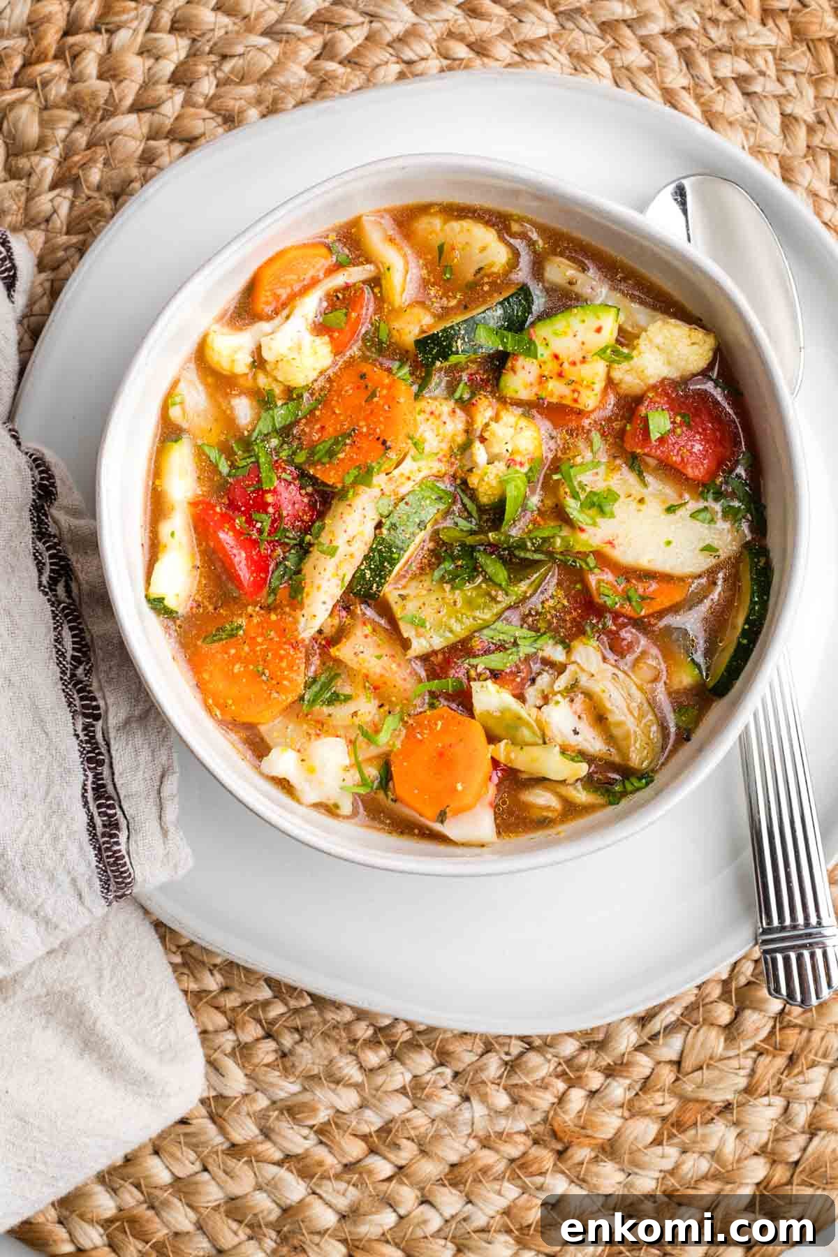 Bowl of colorful chunky veggie soup with fresh herbs.